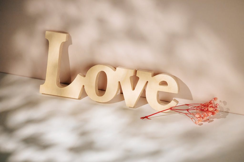 A wooden 'Love' sign with delicate dried flowers, beautifully lit by soft sunlight. Ideal for romantic or decorative themes.
