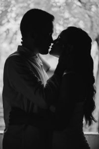 Silhouette of a couple in a romantic embrace and kiss, set against an outdoor backdrop.